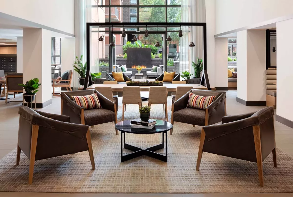 Resident lounge with armchairs, coffee tables, large windows, and indoor plants.