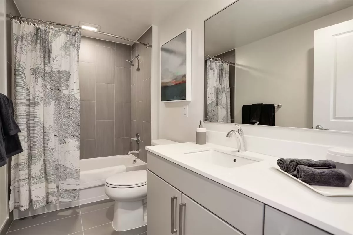 Bathroom with single vanity, mirror, toilet, and tub with tiled surround.