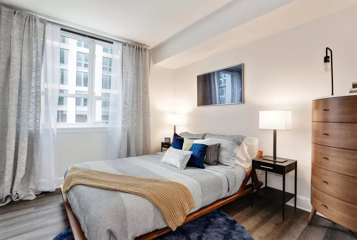 Bedroom with queen bed, nightstands, dresser, area rug, and large window.