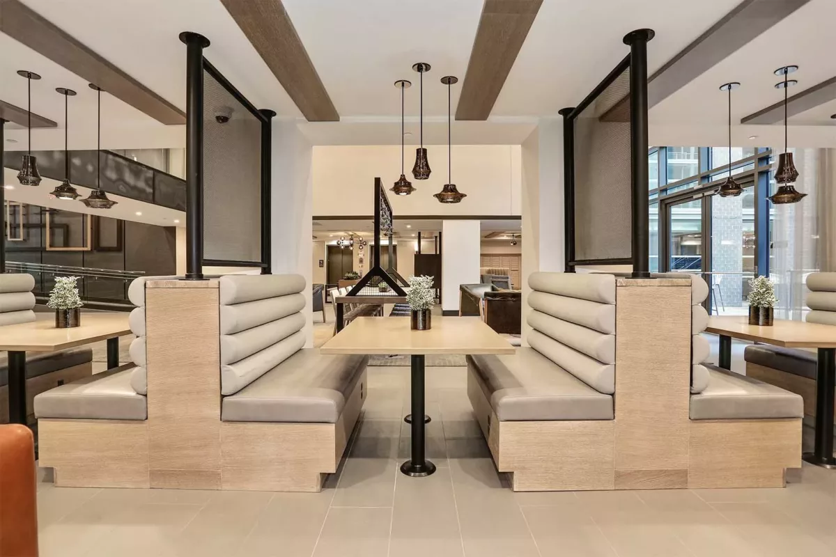 Co‑working lounge with long tables, bench seating, pendant lights, and wood beams.