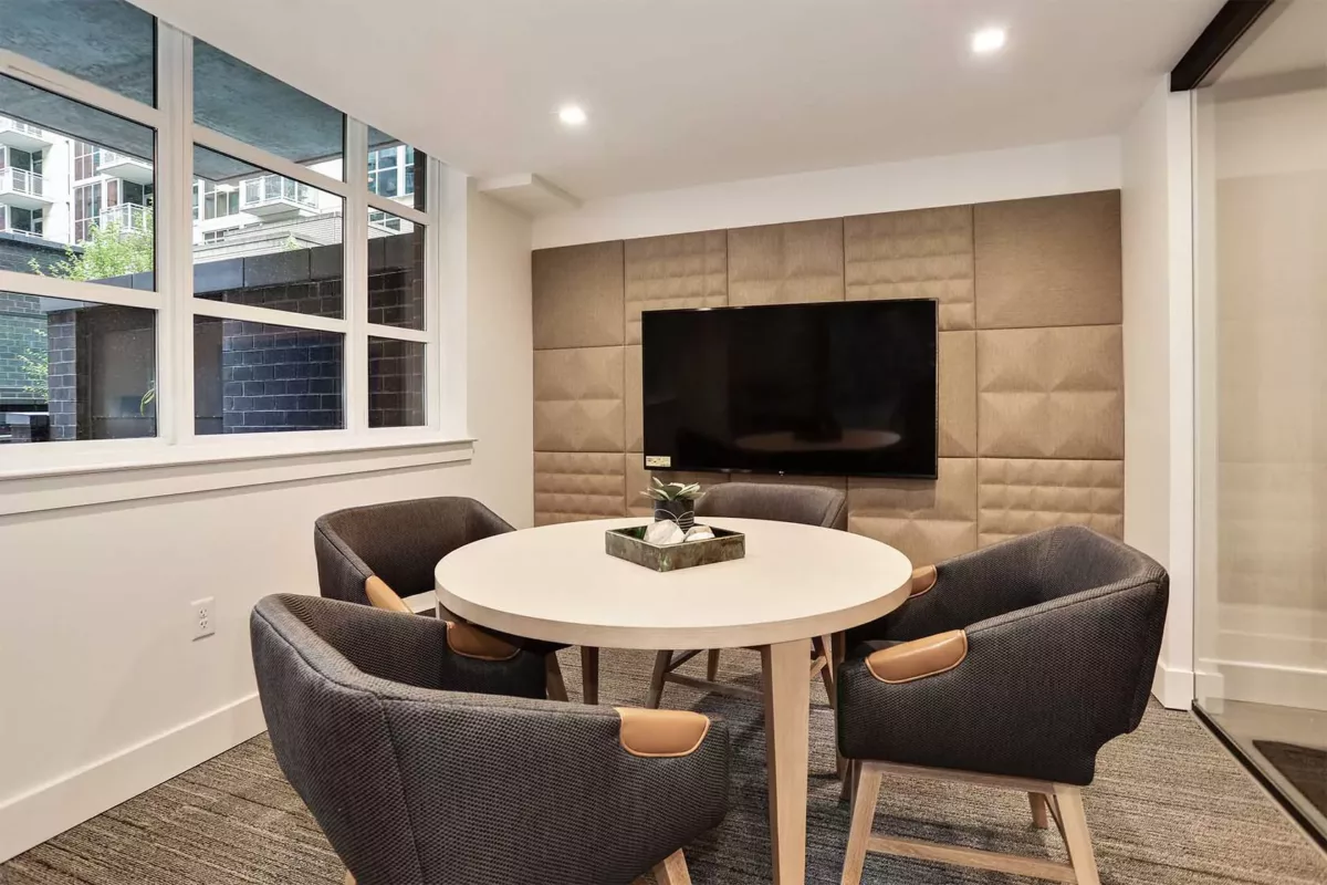 Small meeting lounge with round table, upholstered chairs, and wall‑mounted TV.