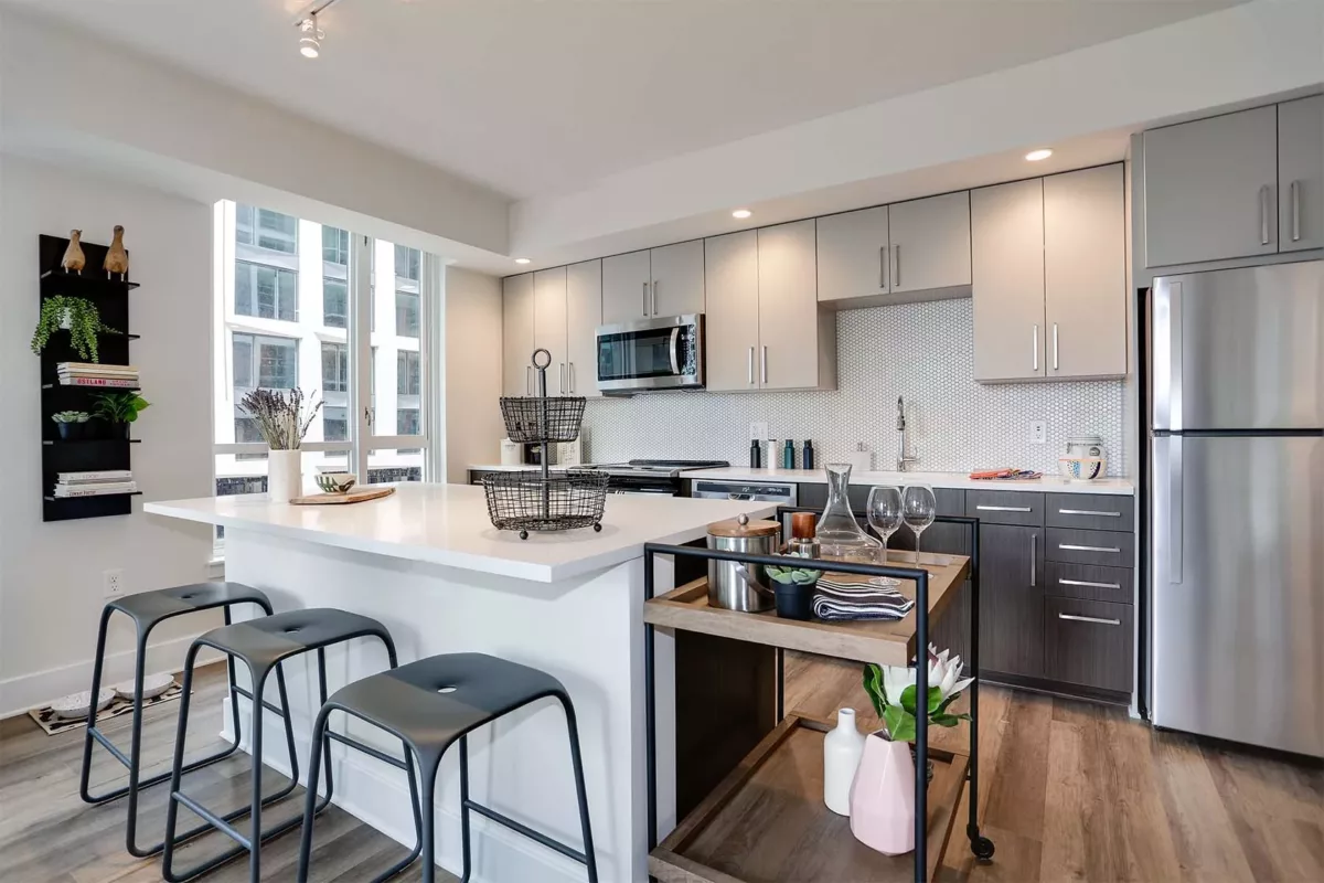 Modern kitchen with white island, gray cabinets, stainless appliances, and three bar stools.