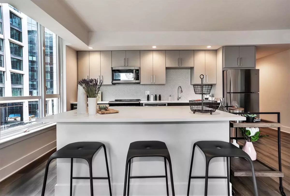 Kitchen island with seating, gray cabinetry, stainless refrigerator, and large window.