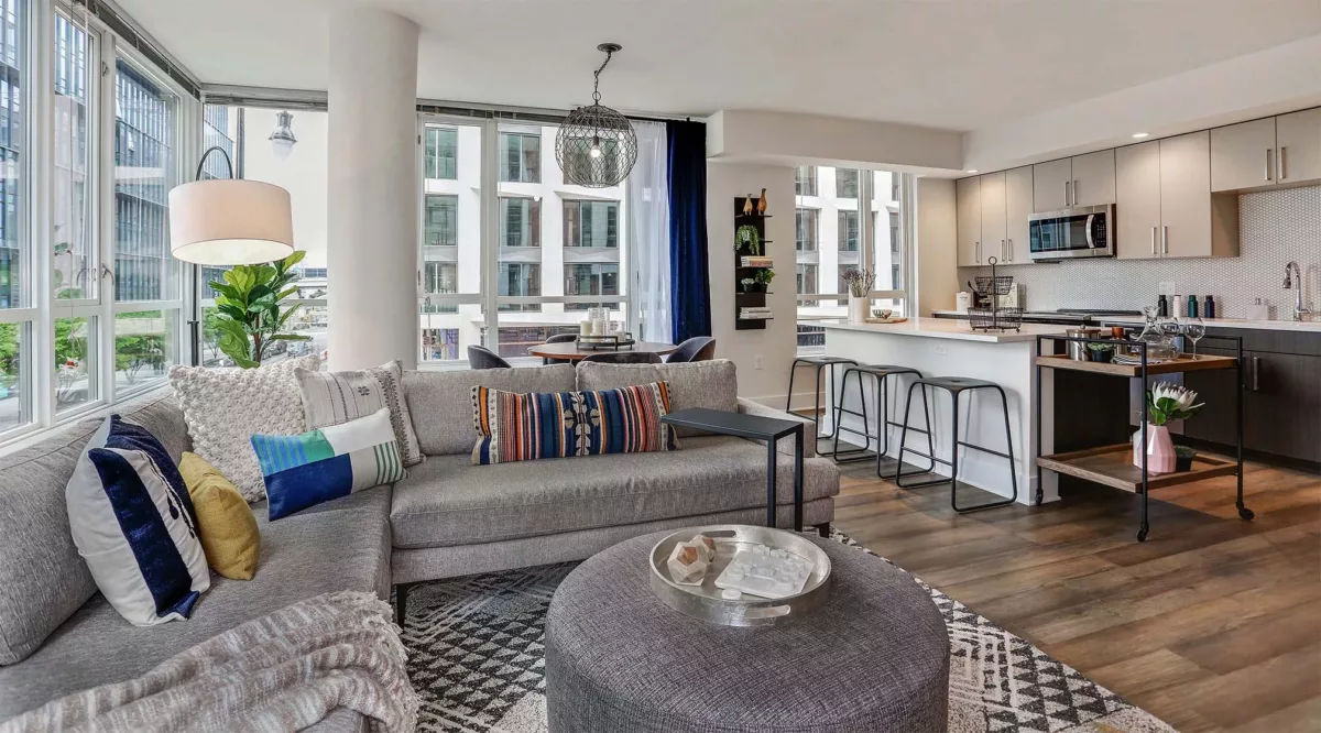 Living room with sectional sofa, patterned rug, floor lamp, and open kitchen beyond.