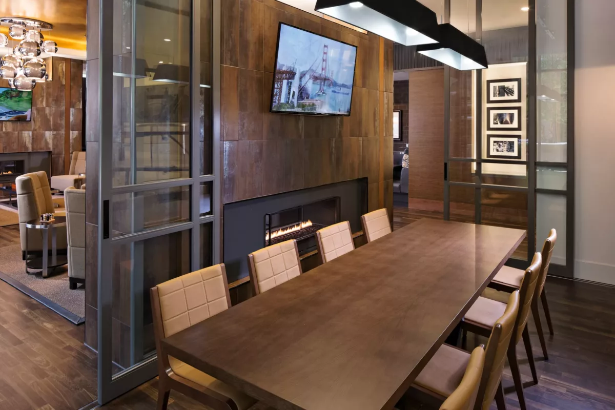 Private meeting room with wood conference table, mounted screen, and glass walls.