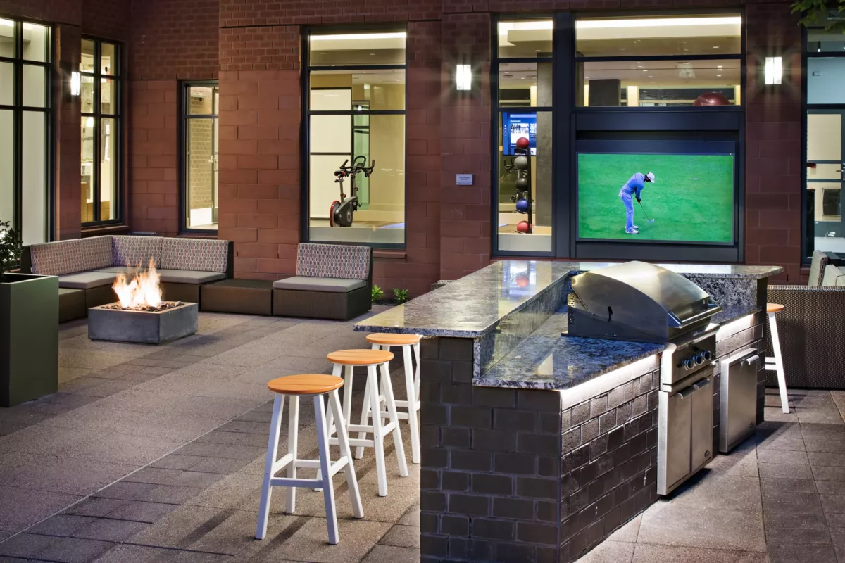 Covered outdoor lounge with sofas, television, and ambient lighting.
