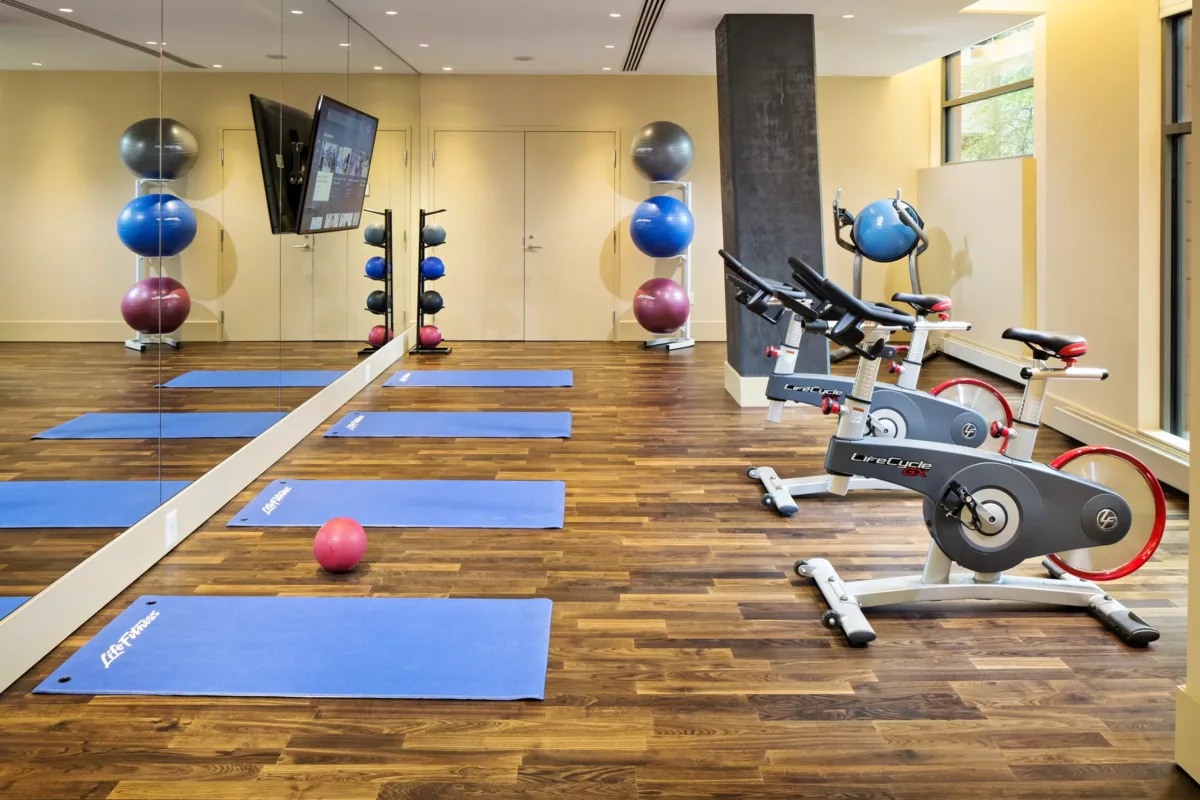Fitness studio with yoga mats, exercise balls, mirrors, and wood flooring.