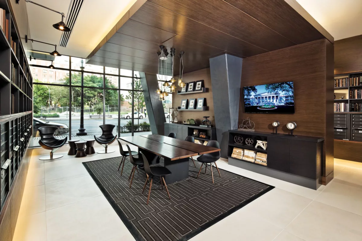 Resident lounge with long communal table, wall‑mounted TVs, and floor‑to‑ceiling windows.