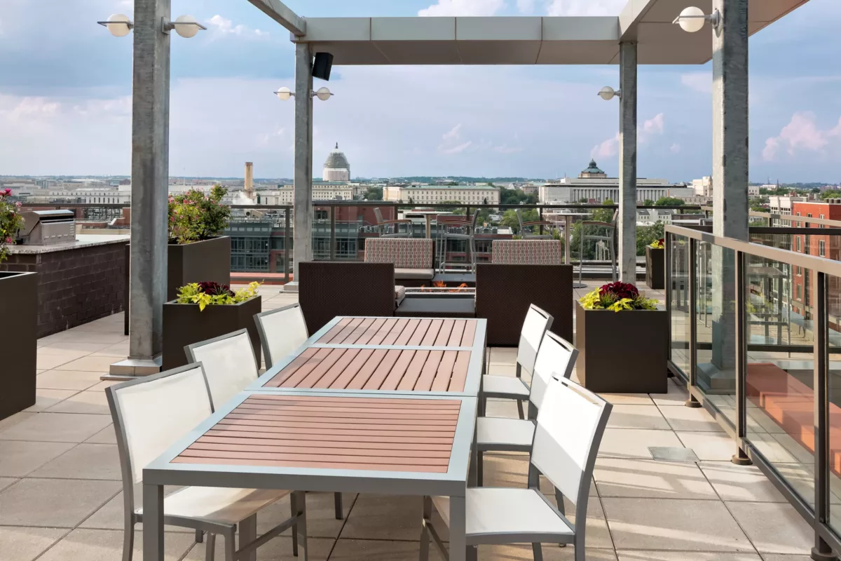 Rooftop terrace with long dining table, seating, pergola, and city views.