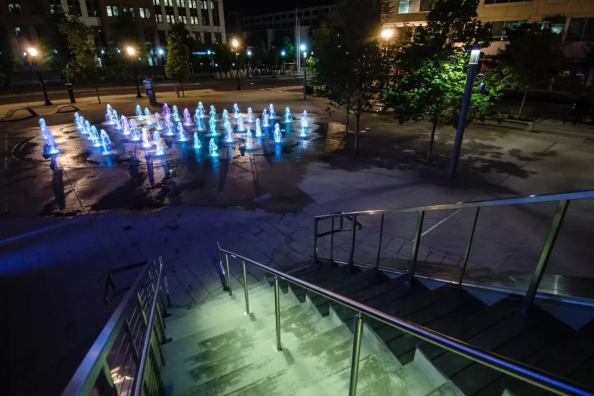 Waterfront boardwalk at night with illuminated railings and reflections on water.