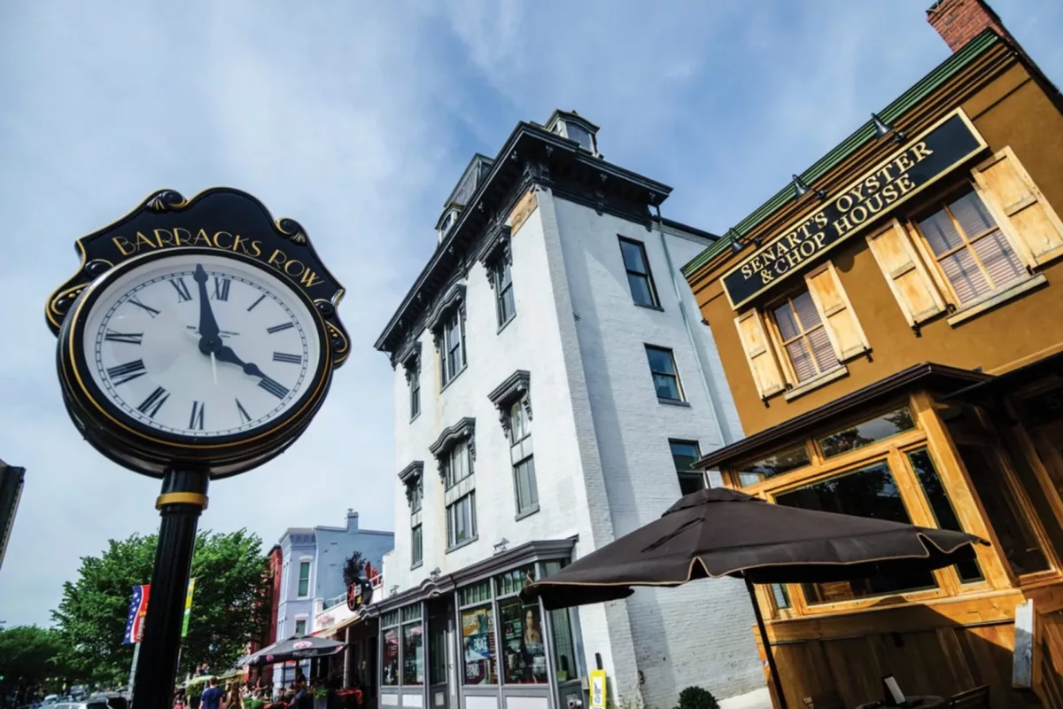Urban street scene with storefronts, hanging clock, and historic buildings.