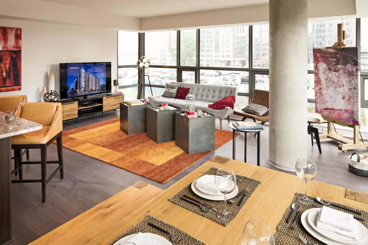 Open living and dining area with sofa, TV console, accent chairs, large windows, and city views.