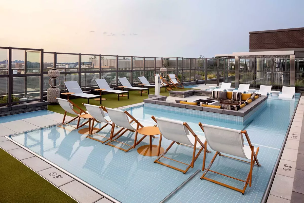 Outdoor pool deck with lounge chairs, umbrellas, and surrounding skyline views.