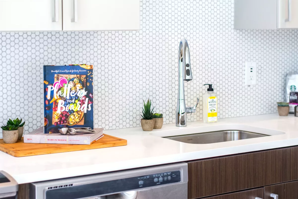 Kitchen sink with gooseneck faucet, hex tile backsplash, and countertop decor.