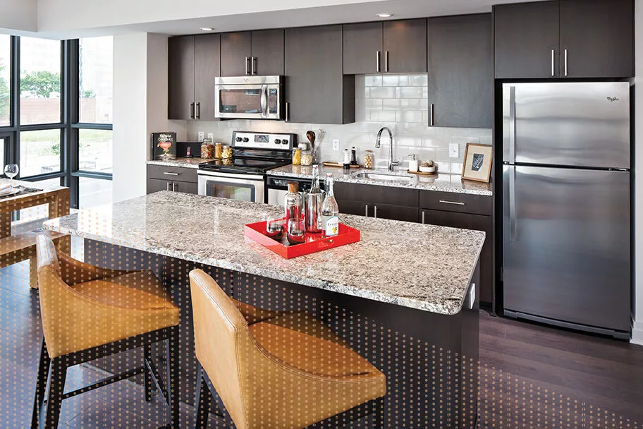 photo of modern kitchen at Parc Riverside apartments in Navy Yard DC. with dark wood cabinets, quartz counters and stainless steel appliances. There is a separate island with two hightop chairs across from the main counter area.